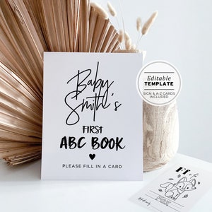 May include: A printable sign for a baby shower or baby's first birthday party. The sign says "Baby Smith's First ABC Book" with a heart symbol and the text "Please fill in a card". The sign is white with black text and is an editable template with A-Z cards included.