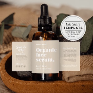 May include: A brown glass bottle with a dropper filled with organic face serum. The label is beige with black text that reads "Organic face serum." The label also includes the brand name, ingredients, directions for use, and website information. The bottle is sitting on a brown surface with a white towel and green leaves.