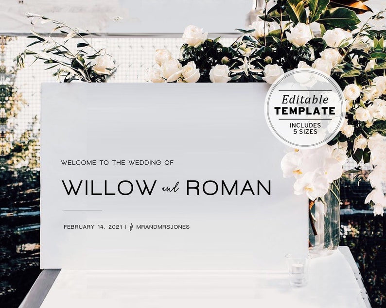 Może przedstawiać: Biały znak ślubny z czarnym tekstem, kt&oacute;ry brzmi "Witamy na ślubie Willow i Romana, 14 lutego 2021, #MRANDMRSJONES". Znak stoi na stole z białymi kwiatami w wazonie.