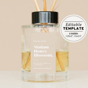 Puede incluir: Una botella de difusor de vidrio transparente con tapa negra y palitos de madera. La etiqueta dice "BRAND NAME", "Madam Honey Blossom", "NOTES OF VANILLA + PEONIES", y "DIFFUSER DE PERFUM".