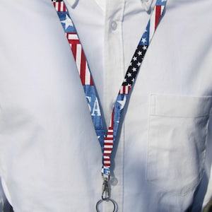 May include: A red, white, and blue lanyard with a silver clip and ring. The lanyard features a patchwork design of American flags and the word "USA".