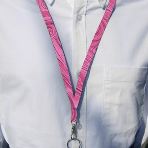 Puede incluir: Un cordón de color rosa y blanco con estampado y un cierre giratorio plateado y un anillo plateado.