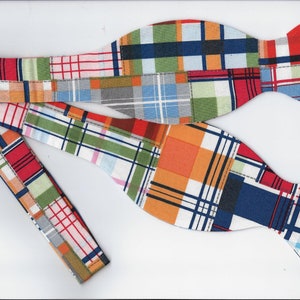May include: A bow tie with a patchwork design featuring a variety of colors, including red, orange, blue, green, and white. The bow tie is made of a plaid fabric and has a unique, handmade look.