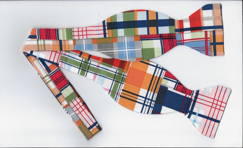 May include: A bow tie with a patchwork design featuring a variety of colors, including red, orange, blue, green, and white. The bow tie is made of a plaid fabric and has a unique, handmade look.