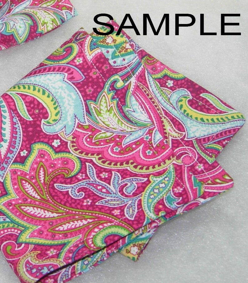 Puede incluir: Un cuadrado de tela con estampado paisley rosa y verde con un borde doblado. La tela tiene un fondo blanco con un estampado paisley rosa, verde y azul.