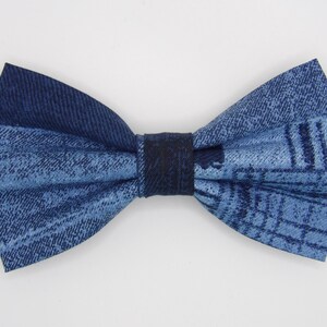 Può includere: Un papillon in denim con un motivo blu chiaro e blu scuro. Il papillon è realizzato in tessuto e ha un cinturino bianco. È un accessorio di moda.