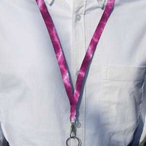 Puede incluir: Un cordón con estampado rosa y blanco con un cierre y un llavero plateados. El cordón se muestra sobre una camisa blanca abotonada.