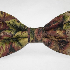 Può includere: Un papillon marrone, verde e oro con un motivo a foglie.