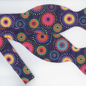 May include: A navy blue bow tie with a colorful, repeating pattern of pink, yellow, green, and blue circles. The circles have a radiating design.