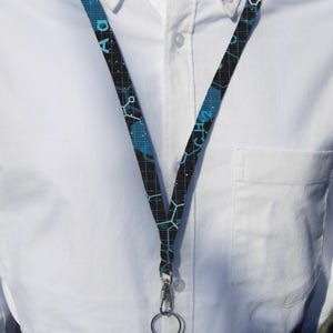 May include: A black lanyard with a blue and white chemical pattern. The lanyard has a silver clip and a silver ring.