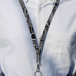 May include: A black and white lanyard with a circuit board pattern. The lanyard has a silver swivel clip and a silver ring.