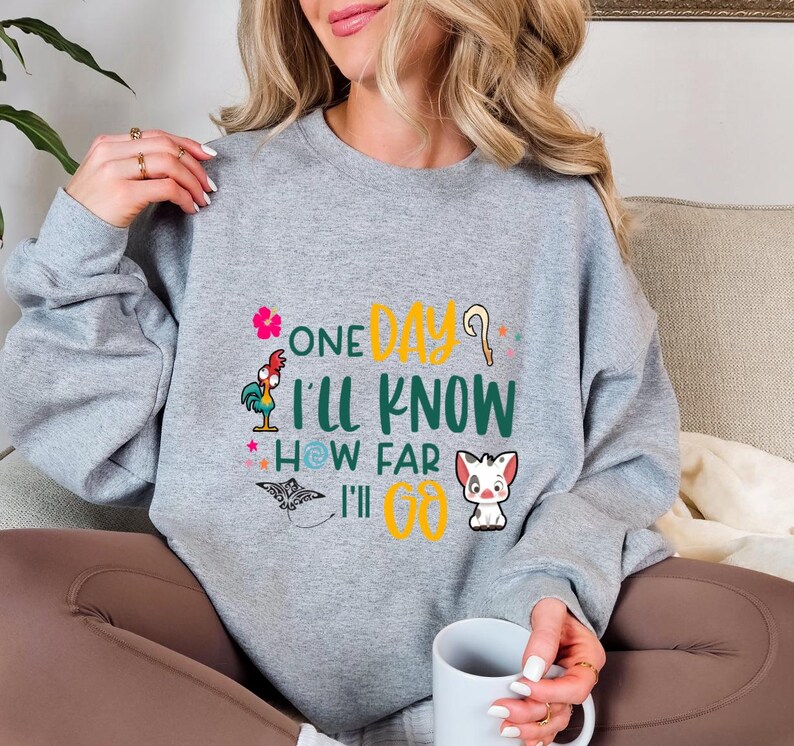 May include: Gray sweatshirt with a colorful graphic print featuring characters from the Disney movie Moana. The text on the shirt reads "One Day I'll Know How Far I'll Go."