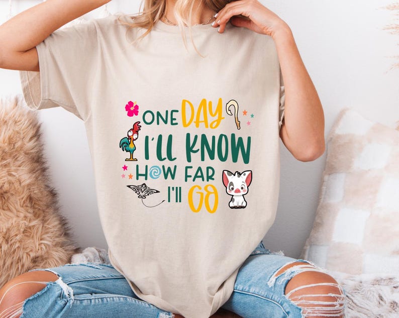 May include: A beige t-shirt with a graphic print of a rooster, a pig, a seashell, and a stick. The text on the shirt reads "One Day I'll Know How Far I'll Go."