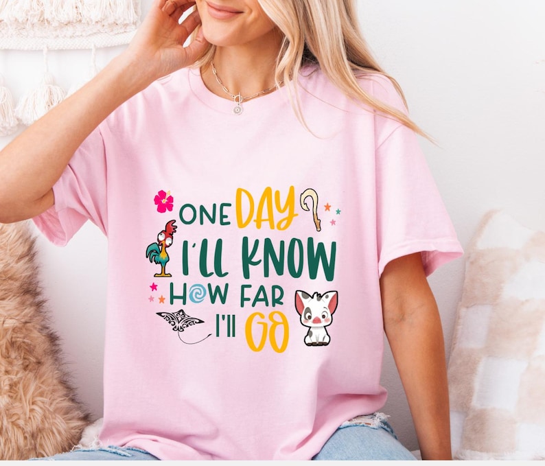 May include: Pink t-shirt with a graphic print of a rooster, a flower, a stick, a star, a swirl, a pig, and the text "One Day I'll Know How Far I'll Go."