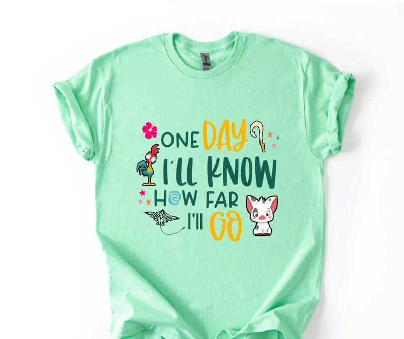May include: A light green t-shirt with a graphic print of a rooster, a flower, a pig, and a seashell. The text on the shirt reads "One Day I'll Know How Far I'll Go."