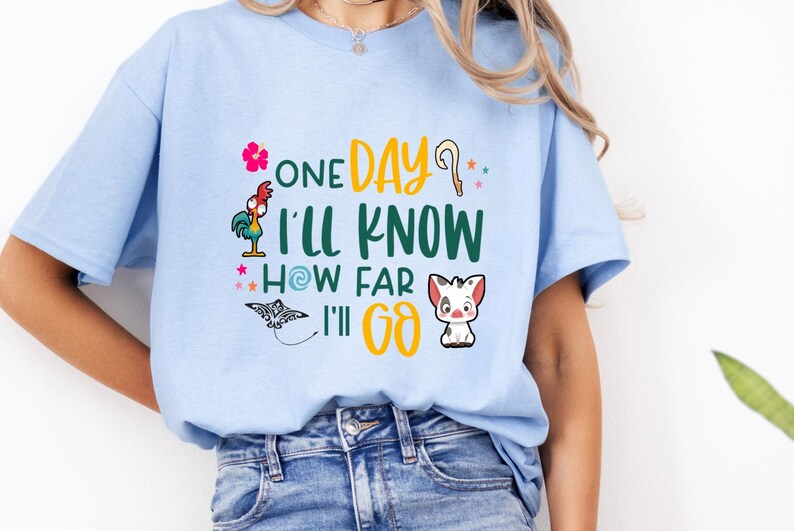 May include: Light blue t-shirt with a graphic print of a rooster, a pig, and a manta ray. The text on the shirt reads "One Day I'll Know How Far I'll Go."