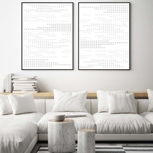 May include: Two black framed abstract art prints with a white background and a pattern of grey squares. The prints are hanging on a white wall above a white sofa with white cushions and two wooden stumps as side tables.