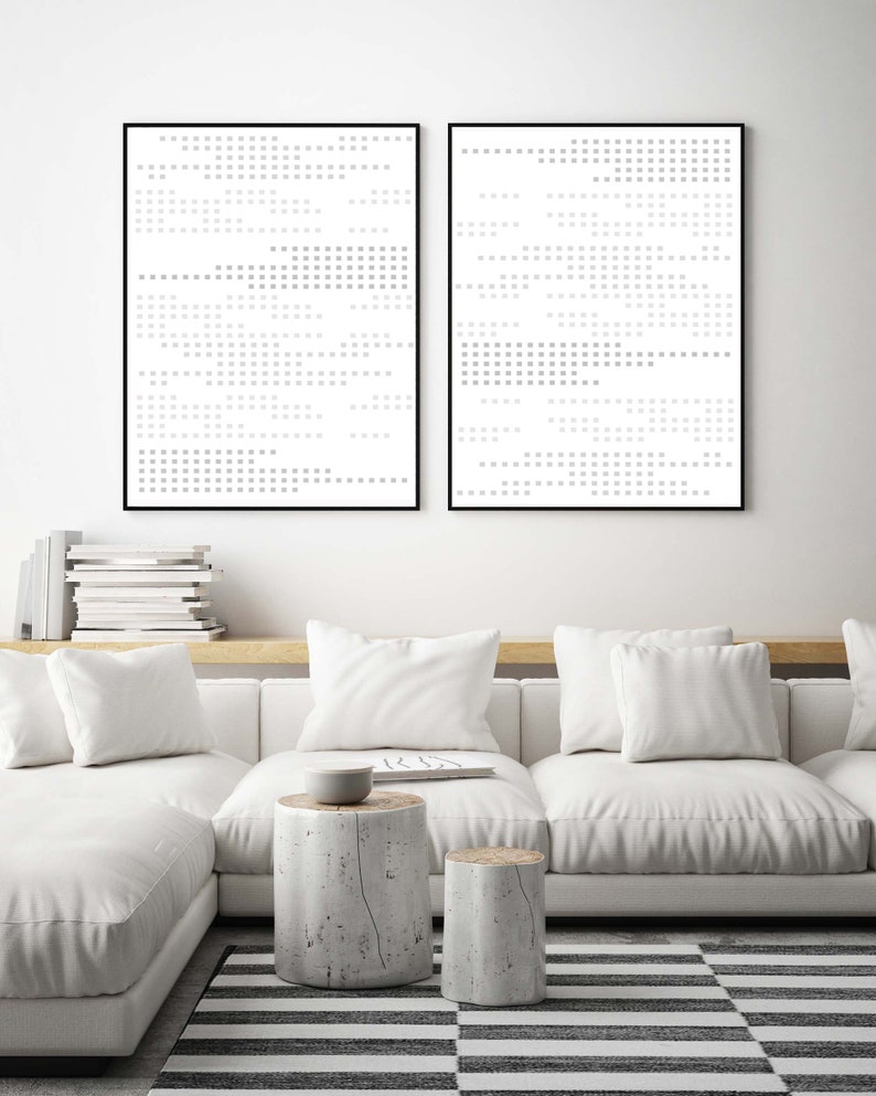 May include: Two black framed abstract art prints with a white background and a pattern of grey squares. The prints are hanging on a white wall above a white sofa with white cushions and two wooden stumps as side tables.