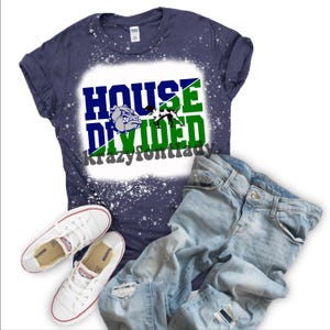 May include: Navy blue t-shirt with the words "HOUSE DIVIDED" in blue and green, along with a bulldog graphic. The shirt is paired with light blue jeans and white sneakers. The text "krazyfontlady" is also visible.