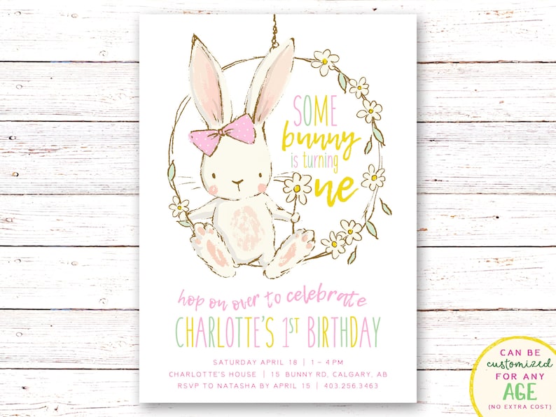 Op de afbeelding: Een roze en wit konijn met een roze strik zit op een schommel gemaakt van een bloemenkrans. De tekst "SOME bunny is turning one" is geschreven in gouden letters. De uitnodiging is voor een eerste verjaardag.