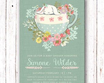 May include: A baby shower invitation with a cute bunny rabbit sitting in a teacup surrounded by flowers. The invitation is on a light blue background with white text that reads "Join us for a baby shower honoring Simone Wilder. Saturday February 18 | 1 PM. Sophia's House | 2012 45 Ave SW. Calgary AB. RSVP to Sophia by February 10 | 403:256 3463. Simone is registered at Babies R Us."
