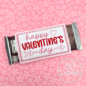 May include: A white felt chocolate bar wrapper with red embroidered text that says "happy Valentine's day" with a heart and arrow.