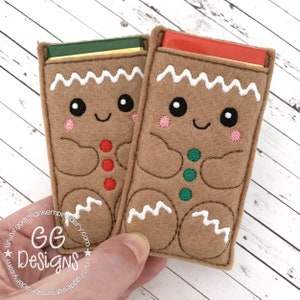 Może przedstawiać: Dwa filcowe woreczki w kształcie piernikowego ludzika z haftowanymi twarzami i guzikami. Woreczki są wypełnione tabliczkami czekolady.