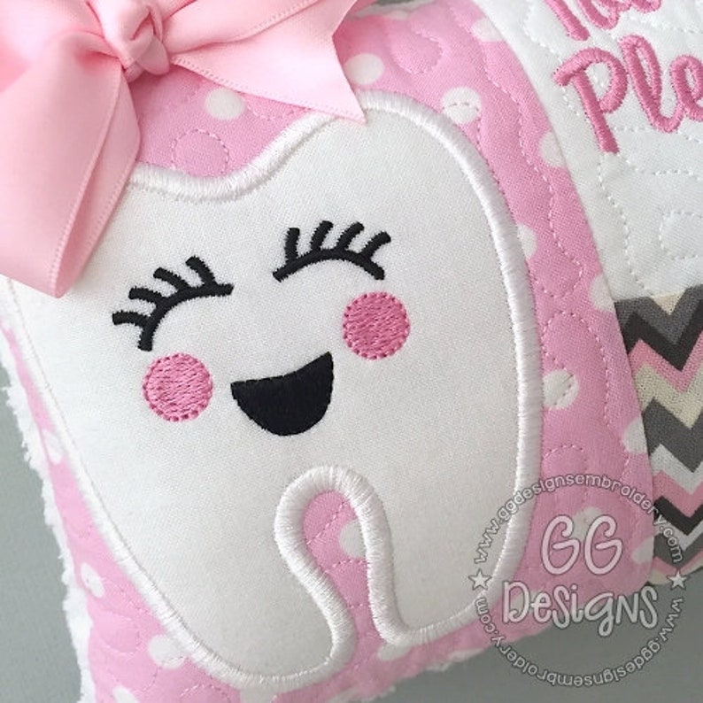 May include: A pink and white tooth pillow with a smiling tooth face embroidered on it. The tooth has pink cheeks and eyelashes. The pillow has a pink polka dot fabric with a white bow on top.