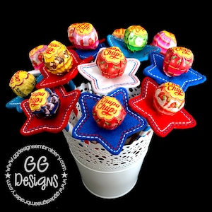 May include: A bouquet of lollipops wrapped in red, white, and blue star-shaped fabric. The lollipops are all wrapped in colorful wrappers with the brand name "Chupa Chups" printed on them.