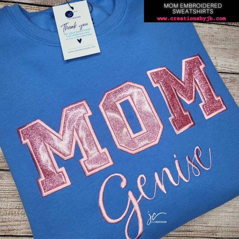 May include: A blue sweatshirt with pink glitter lettering that reads "MOM Genise".