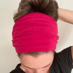 May include: A bright pink headband made of soft fabric. The headband is worn by a person with brown hair pulled back in a bun.
