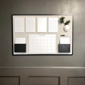 May include: A black framed corkboard with a calendar, notepads, and a small vase with a plant. The calendar is labeled "November".