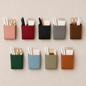 May include: Nine rectangular faux leather desk organizers in various colors including pink, red, black, gray, brown, dark green, light blue, olive green, and tan. Each organizer holds stationery items like pens, scissors, and small spiral notebooks.