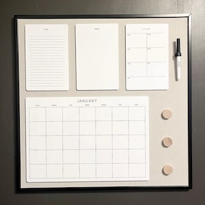 May include: A black framed dry erase board with a calendar, to-do list, notes section, and weekly planner. The board has three wooden push pins.