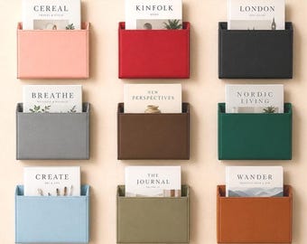 May include: Nine rectangular wall-mounted storage pockets in various solid colors including pink, red, black, gray, brown, green, light blue, olive, and orange. Each pocket holds a book or magazine with titles like Cereal, Kinfolk, and Wander.