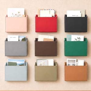 May include: A set of nine rectangular wall-mounted storage pockets in various colors including light pink, red, black, gray, brown, green, light blue, beige, and tan. Each pocket holds assorted white cards, envelopes, and photographs.