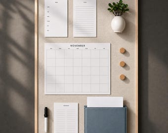 May include: A rectangular beige fabric bulletin board with a light wood frame. It features a white November calendar, a menu list, a to-do list, a grocery list, a black marker, three small wooden circular magnets, a blue pocket, and a white vase.