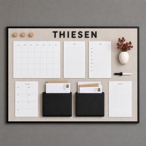 May include: A rectangular wall-mounted organization board with a black frame and beige fabric surface. It features the name THIESEN in black letters, a monthly calendar, a to-do list, a menu, a weekly planner, a grocery list, two black pockets, and a marker.