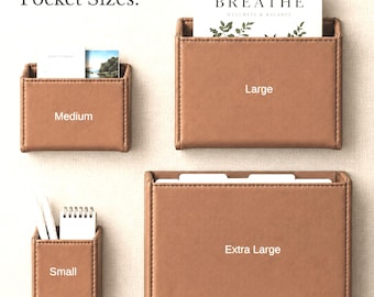 May include: Four tan rectangular wall-mounted pockets labeled Small, Medium, Large, and Extra Large. The pockets feature stitched edges and hold various items including a notepad and a card with the text BREATHE WELLNESS & BALANCE.