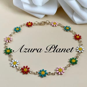 May include: A gold-tone chain bracelet featuring daisy flower charms in various colours. The flowers have red, white, green, pink, and teal petals with yellow centres. The text "Azura Planet" is visible.