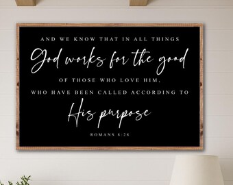 May include: A framed black wall art with white script that reads "God works for the good". The art is displayed above a wooden cabinet with a lamp, a plant, and a woven basket. The room has a neutral color palette.