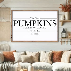 May include: A white sign with black text that reads 'From Fresh Pumpkins For Pies Or Carving Pick Your Own 10¢ Per LB.' The sign is hanging on a white wood wall with a rustic wood shelf above it. There is a couch with pillows in the foreground. The couch is white with orange and brown pillows. There is a coffee table in front of the couch with a basket of orange pumpkins on it.