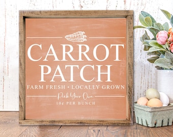May include: A wooden sign with a peach background and white text that reads "Carrot Patch Farm Fresh Locally Grown Pick Your Own 1.00$ Per Bunch". The sign is sitting on a wooden table with a vase of flowers and a wooden bunny.