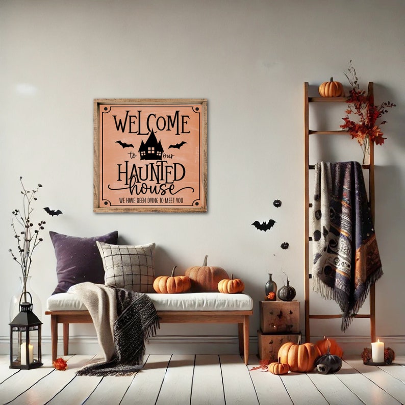 May include: A wooden sign with a peach background and black lettering that reads "Welcome to our Haunted House. We have been dying to meet you." The sign is hanging on a white wall in a room decorated for Halloween with pumpkins, bats, and a blanket.