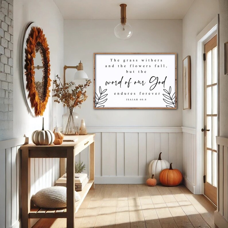 May include: A white framed sign with black text and floral accents. The text reads "The grass withers and the flowers fall, but the word of our God endures forever. Isaiah 40:8".