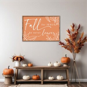 May include: A wooden sign with an orange background and white lettering that reads "Fall for Jesus he never leaves". The sign is surrounded by fall-themed decorations, including pumpkins and fall leaves.
