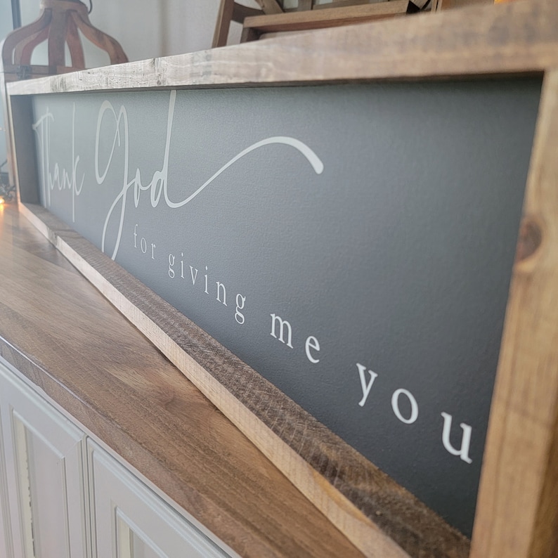 May include: A rustic wooden framed sign with a gray background and white text that reads "Thank God for giving me you".
