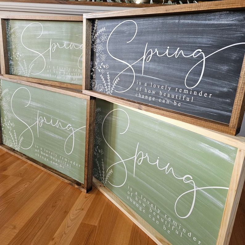 May include: Three wooden signs with a spring theme. Each sign has a white painted floral design and the text "Spring is a lovely reminder of how beautiful change can be". The signs are painted in different colors: black, green, and a light green.