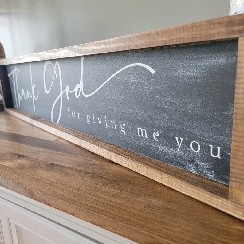 May include: A rustic wooden sign with a black background and white lettering. The sign reads "Thank God for giving me you".