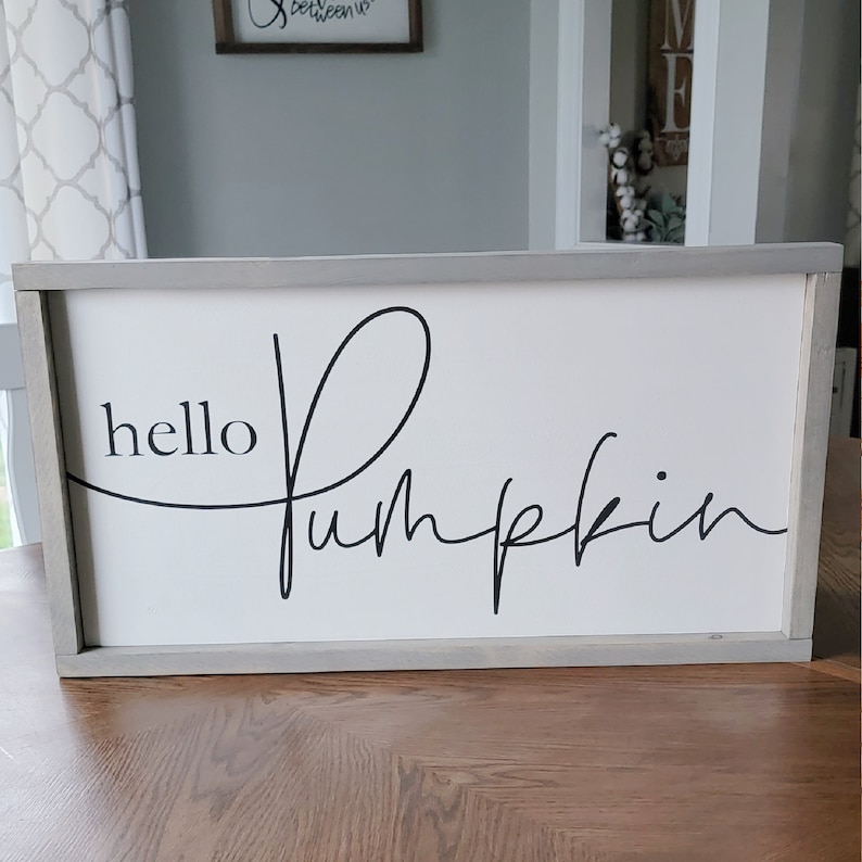 Puede incluir: Un letrero de madera blanco con marco gris, con el texto "hello pumpkin" en letra cursiva negra.